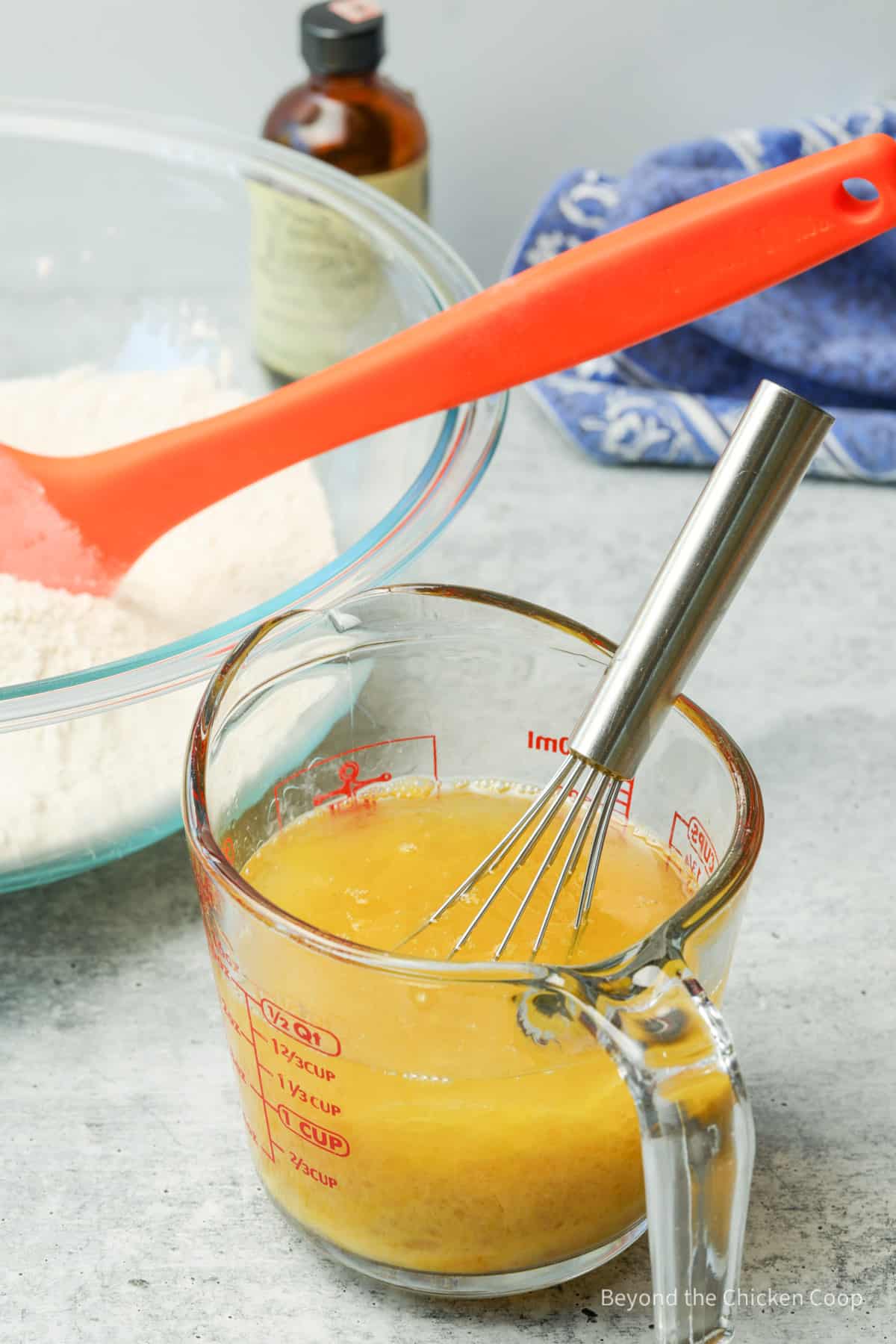 Egg and oil combined in a glass measuring cup with a whisk. 
