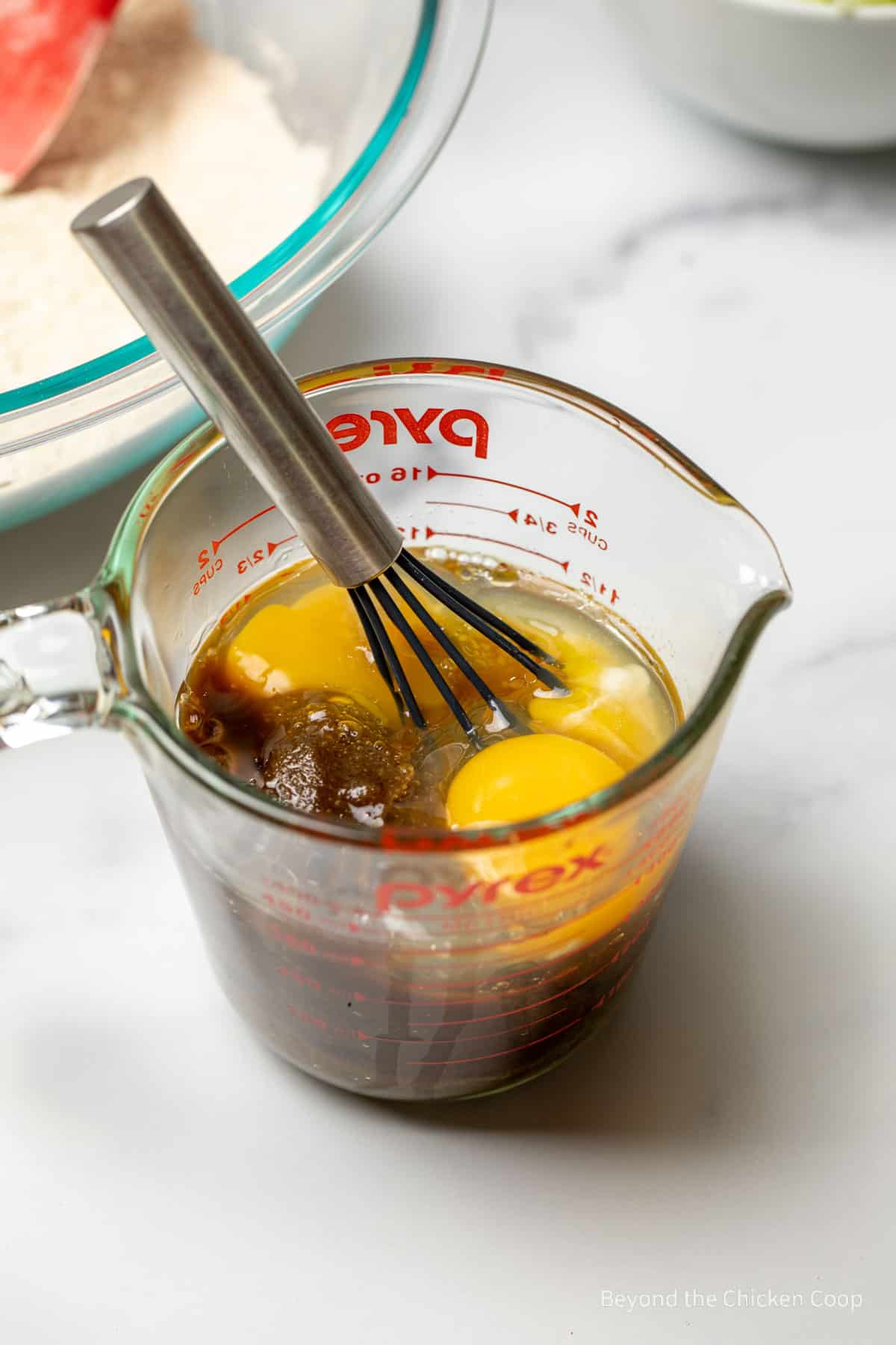 Eggs and brown sugar in a glass measuring cup with a whisk. 