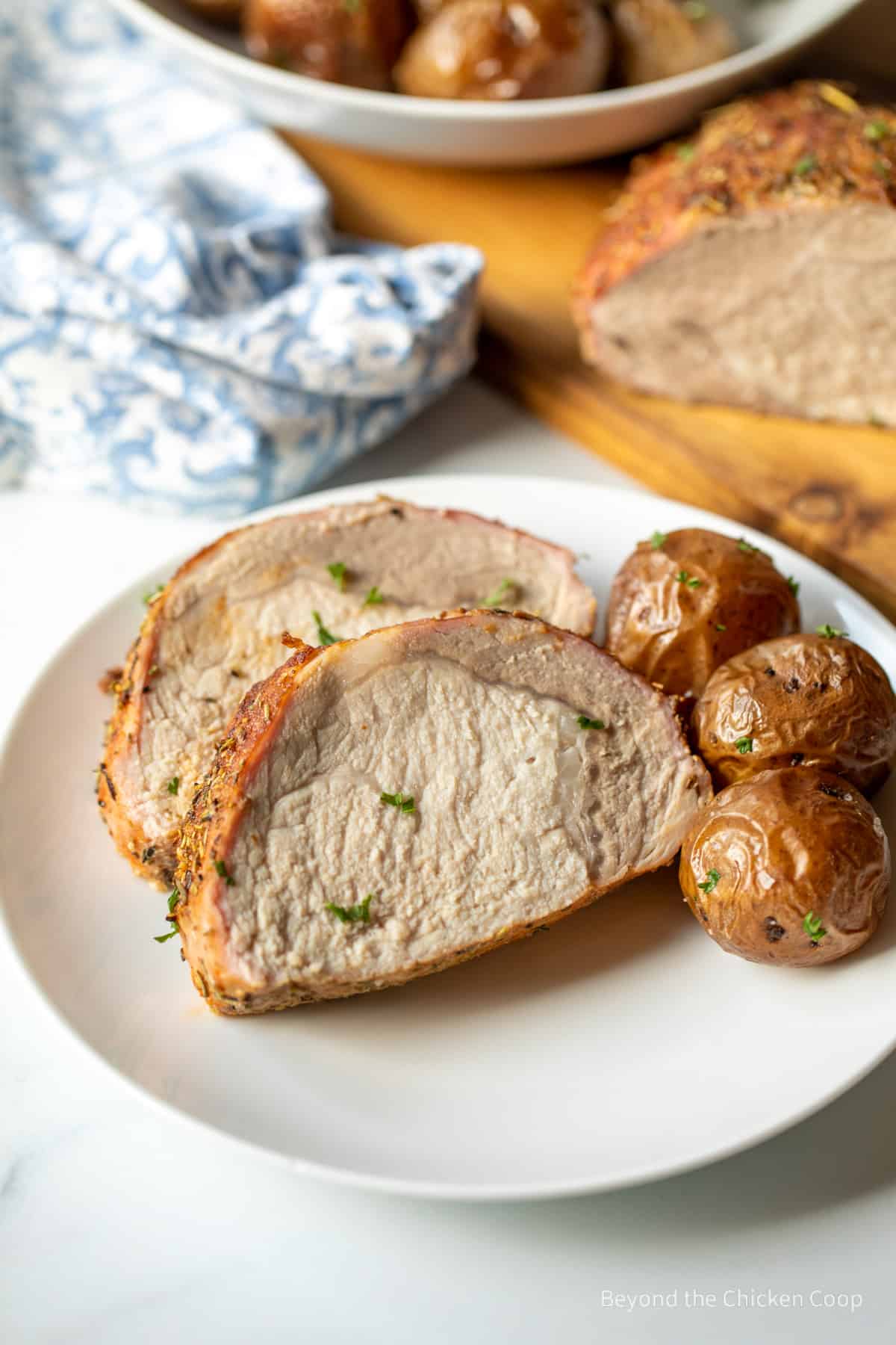 Sliced pork roast and baby potatoes on a white plate. 