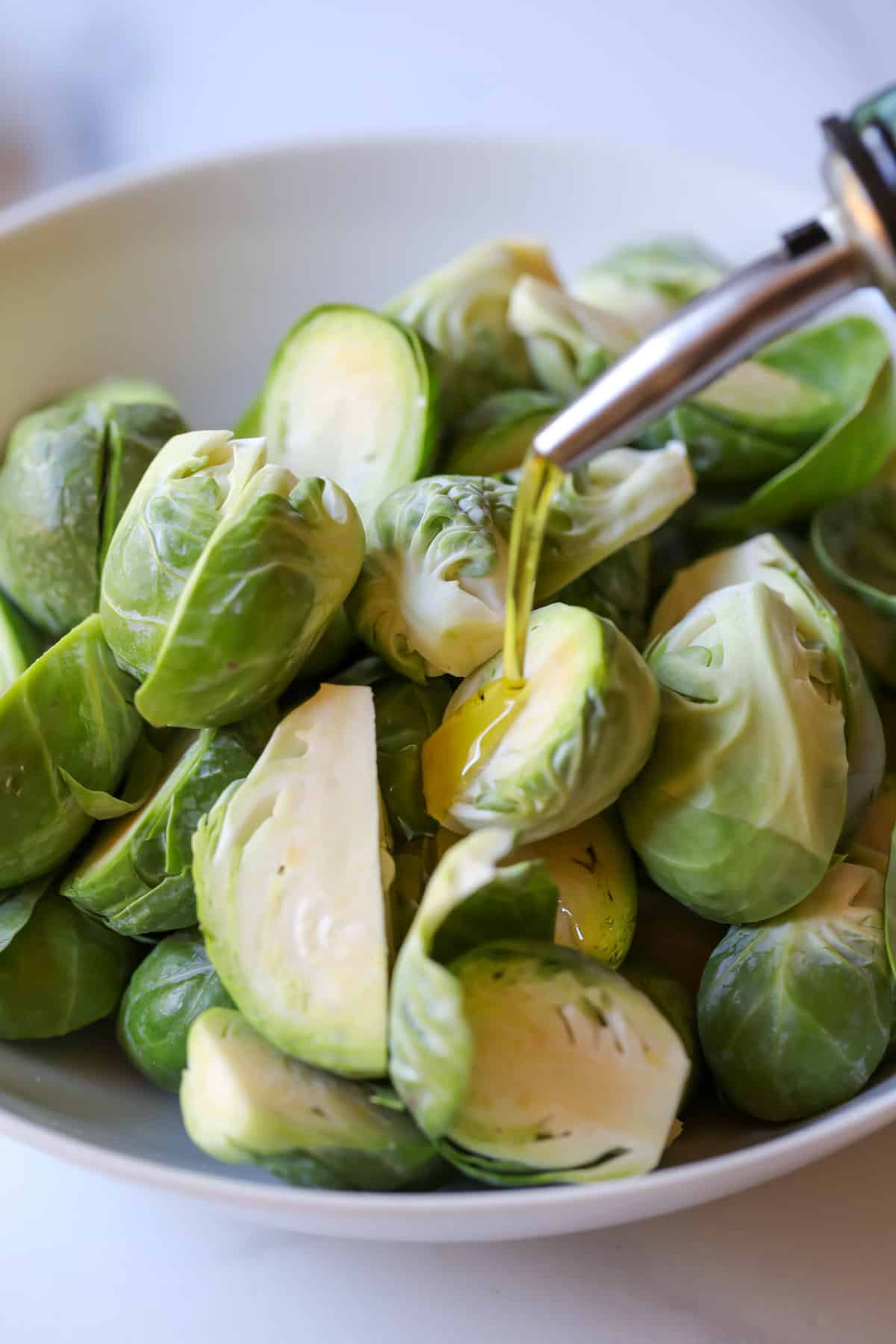 Pouring olive oil over green brussels sprouts. 