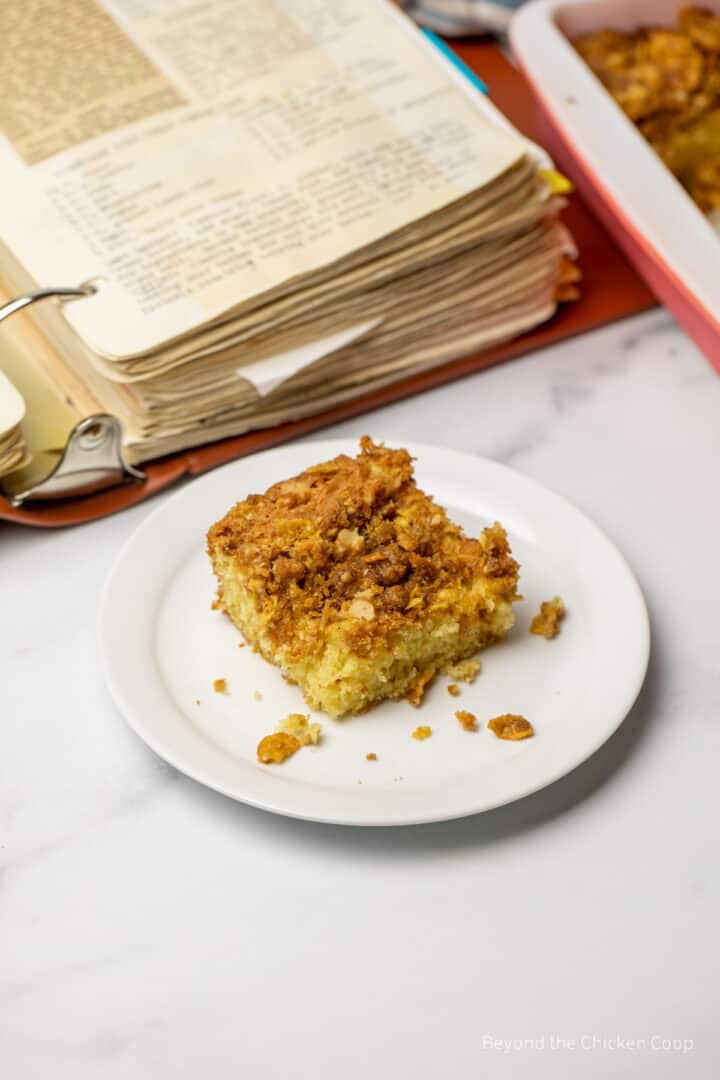 A slice of cake next to a large recipe book.