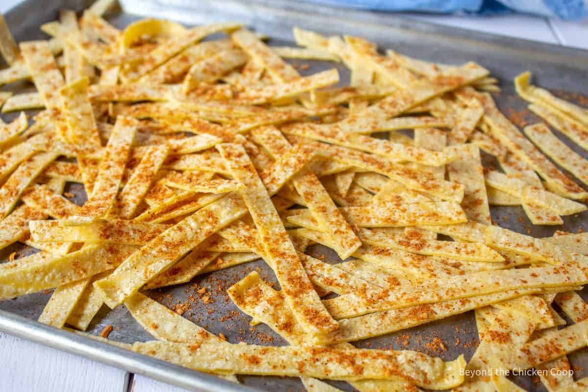 Tortilla strips covered with seasoning on a baking sheet. 