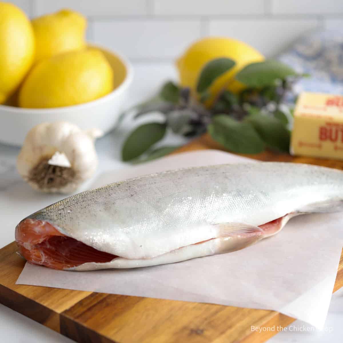 A whole trout next to fresh lemons, garlic and sage leaves. 