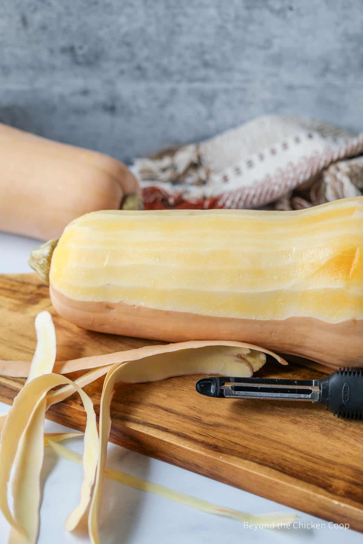 Peeling a butternut squash with a vegetable peeler.