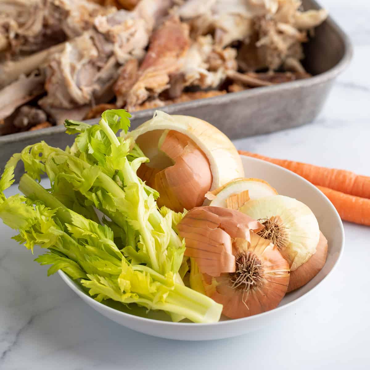 A bowl filled with celery tops, and onions with a pan of turkey in the back. 