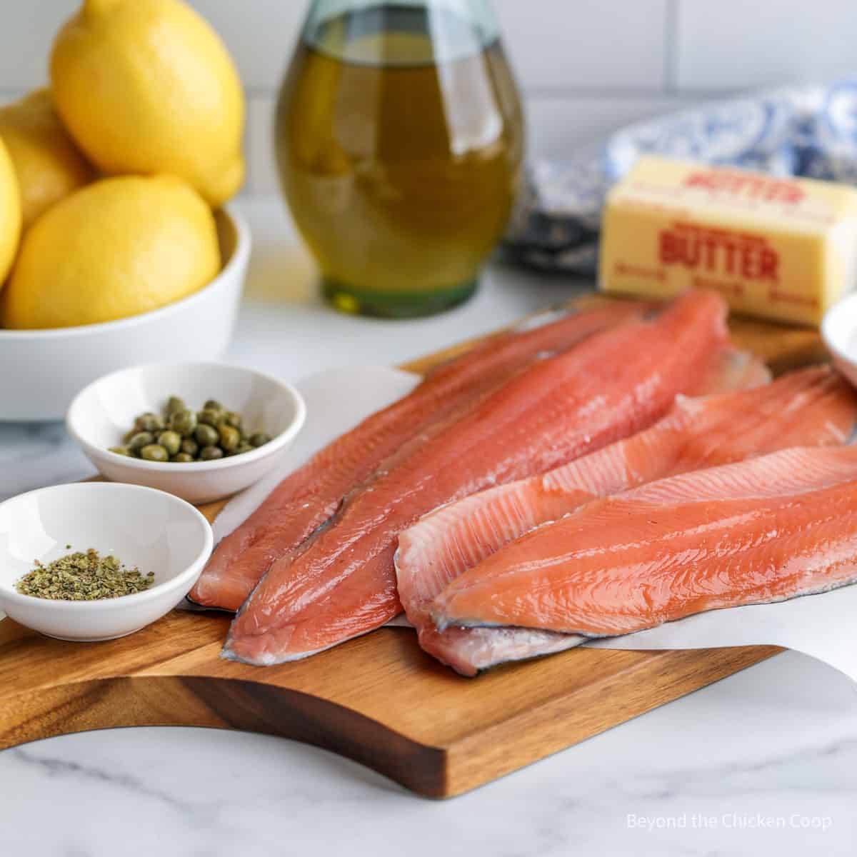 Fillets of trout next to butter, capers, lemons and seasoning. 