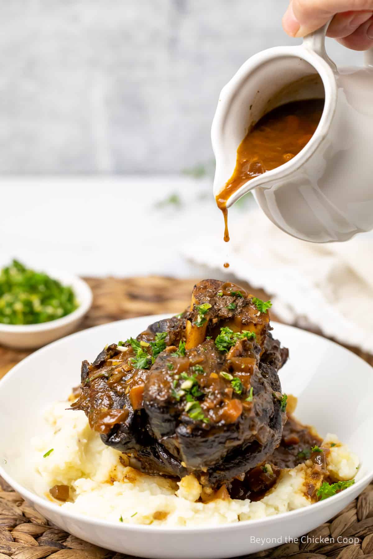 Pouring gravy over the top of osso buco. 