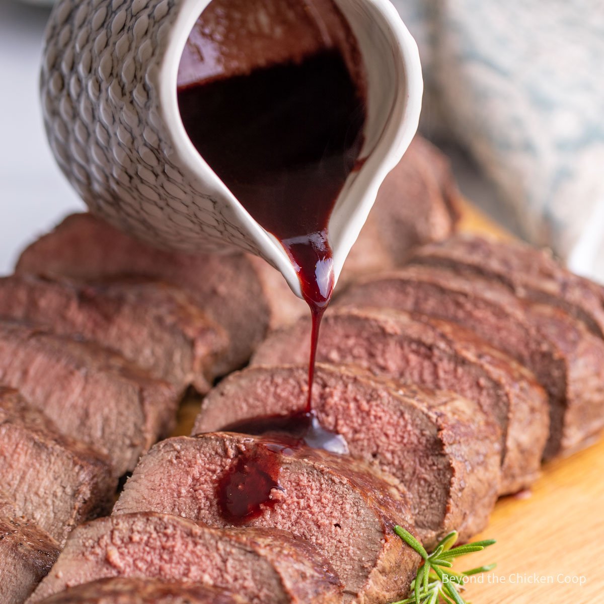 A red wine sauce being poured over sliced red meat.