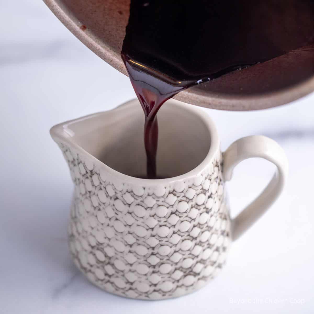 A red wine sauce being poured into a small pitcher.