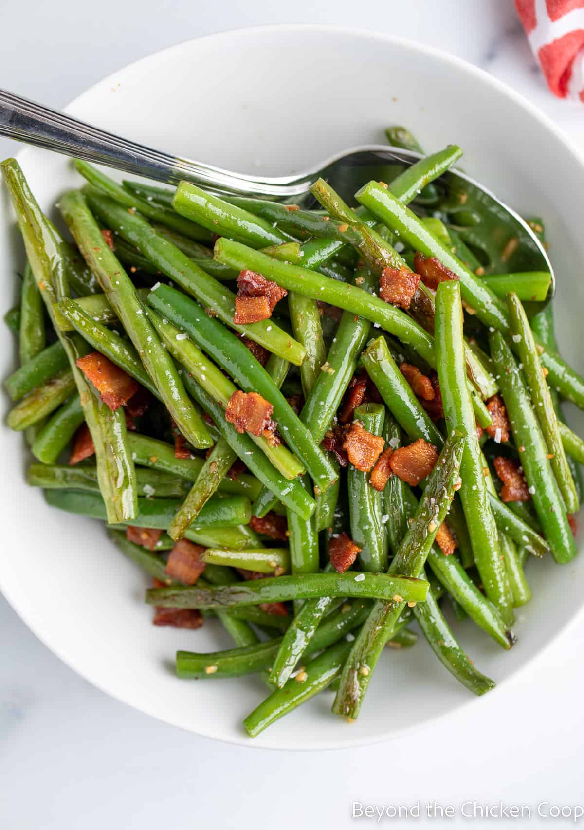 A white plate piled with green beans and bacon. 