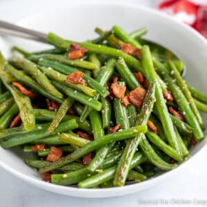 Green beans with bits of bacon in a white bowl.