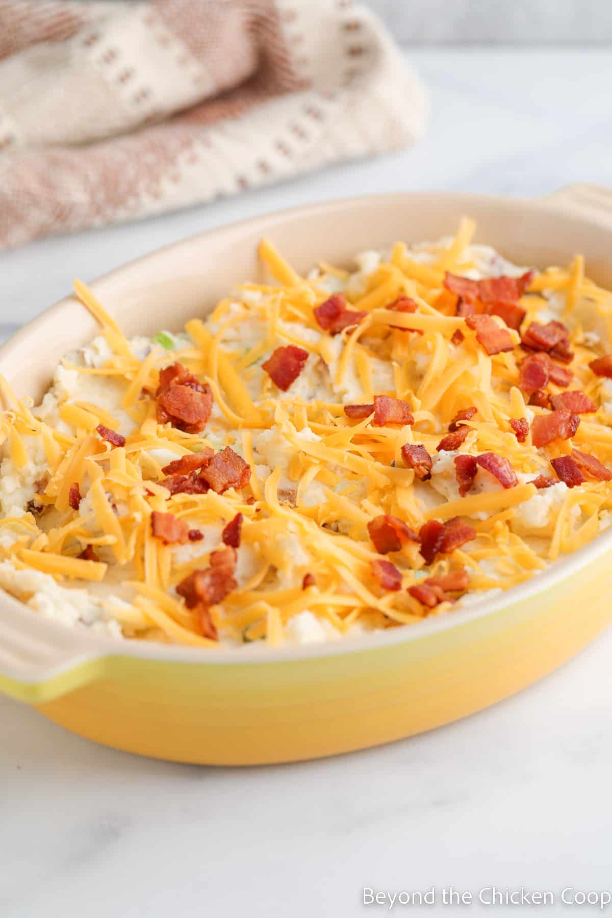 An unbaked casserole topped with cheese and bacon.