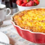 A red pie dish filled with an egg casserole.