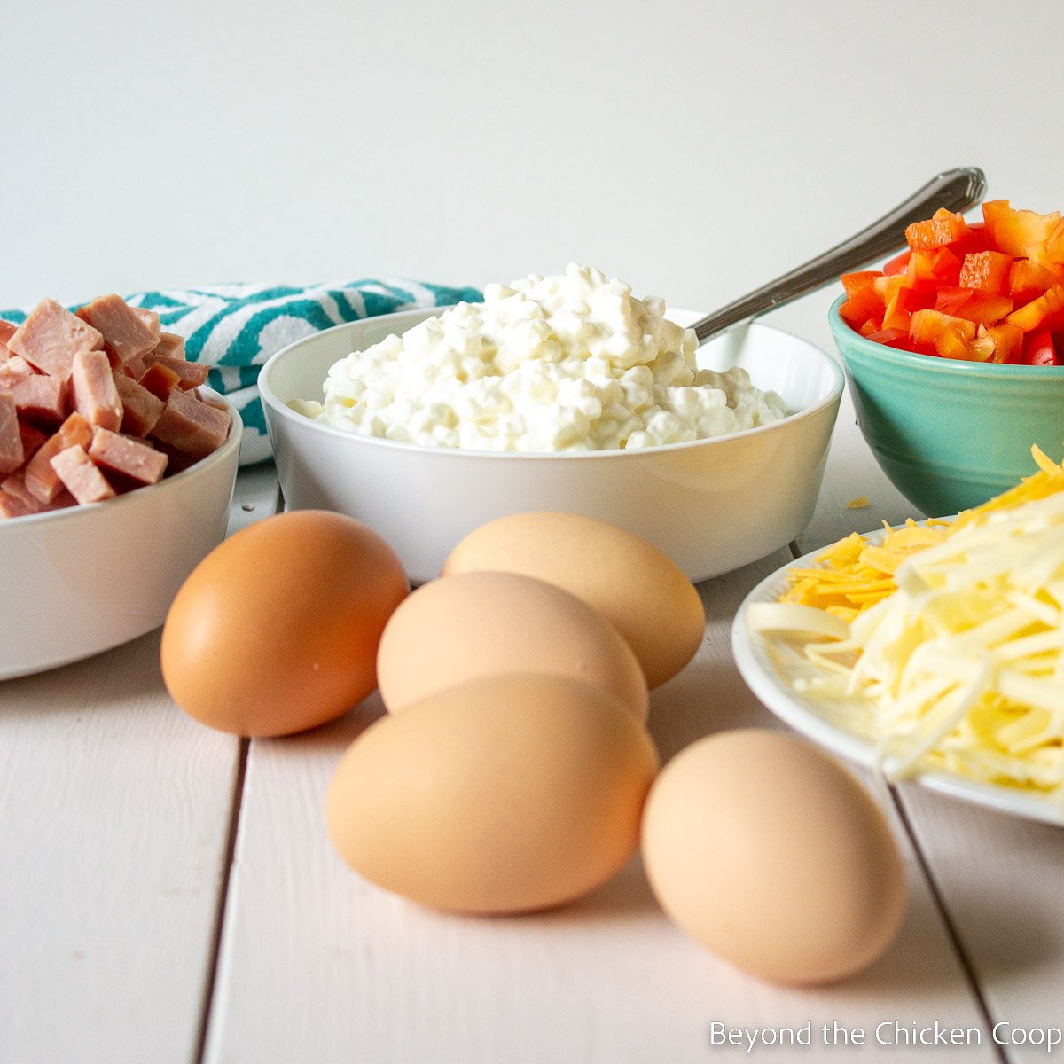 Fresh eggs next to bowls of cheese and ham. 