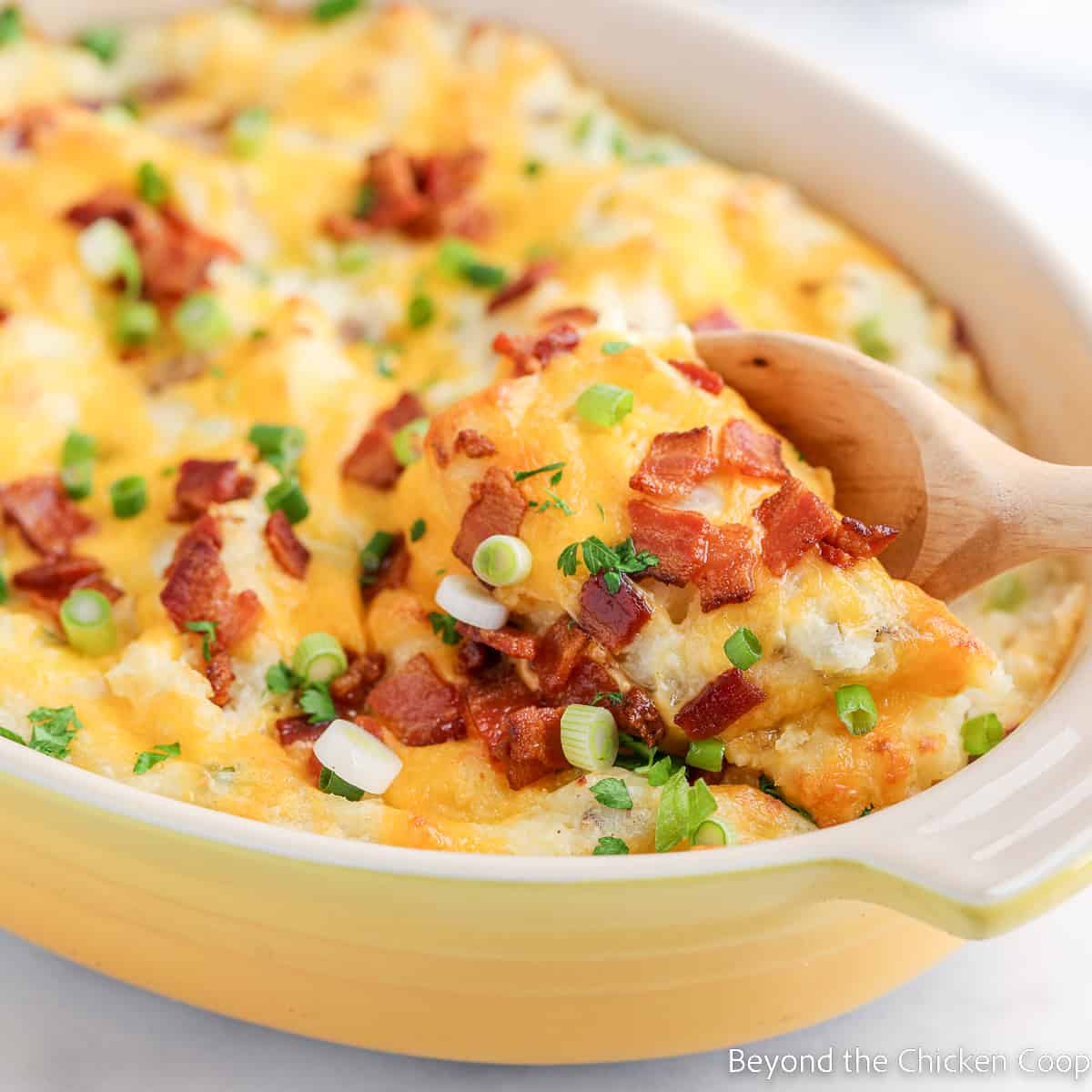 Mashed potatoes topped with cheese and bacon in a yellow dish.