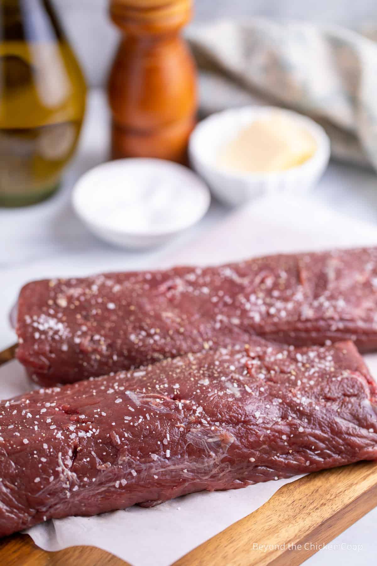 Two venison roasts sprinkled with salt on a board.