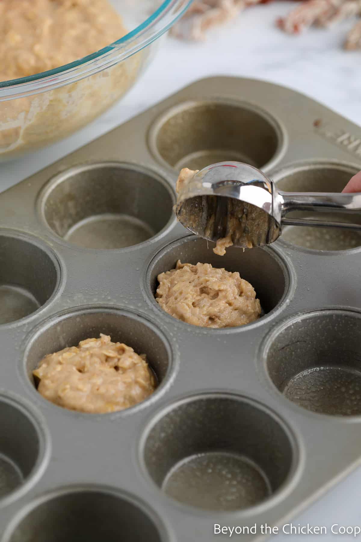Scooping muffin batter into a muffin tin. 