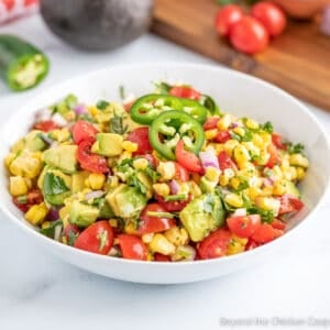 Corn, tomatoes and avocados in a white bowl.