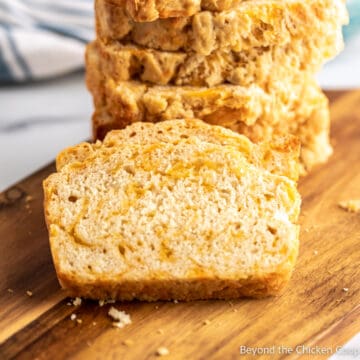 A slice of beer bread with cheddar cheese on a board.