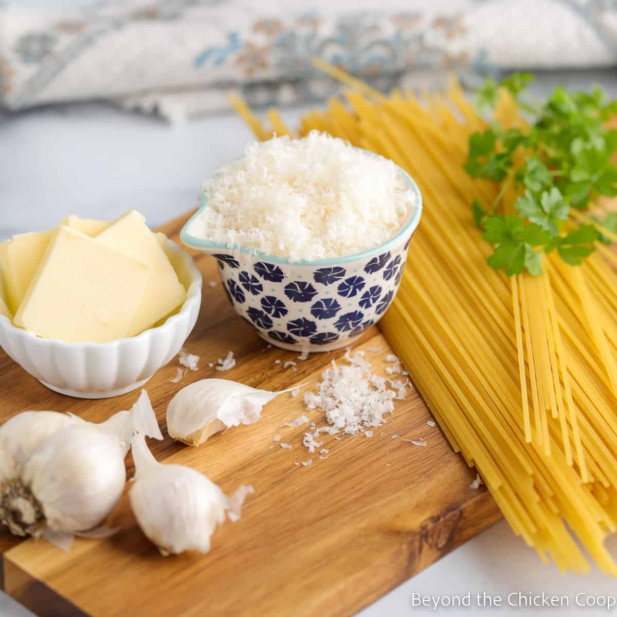 Spaghetti noodles next to a bowl of parmesan and butter.
