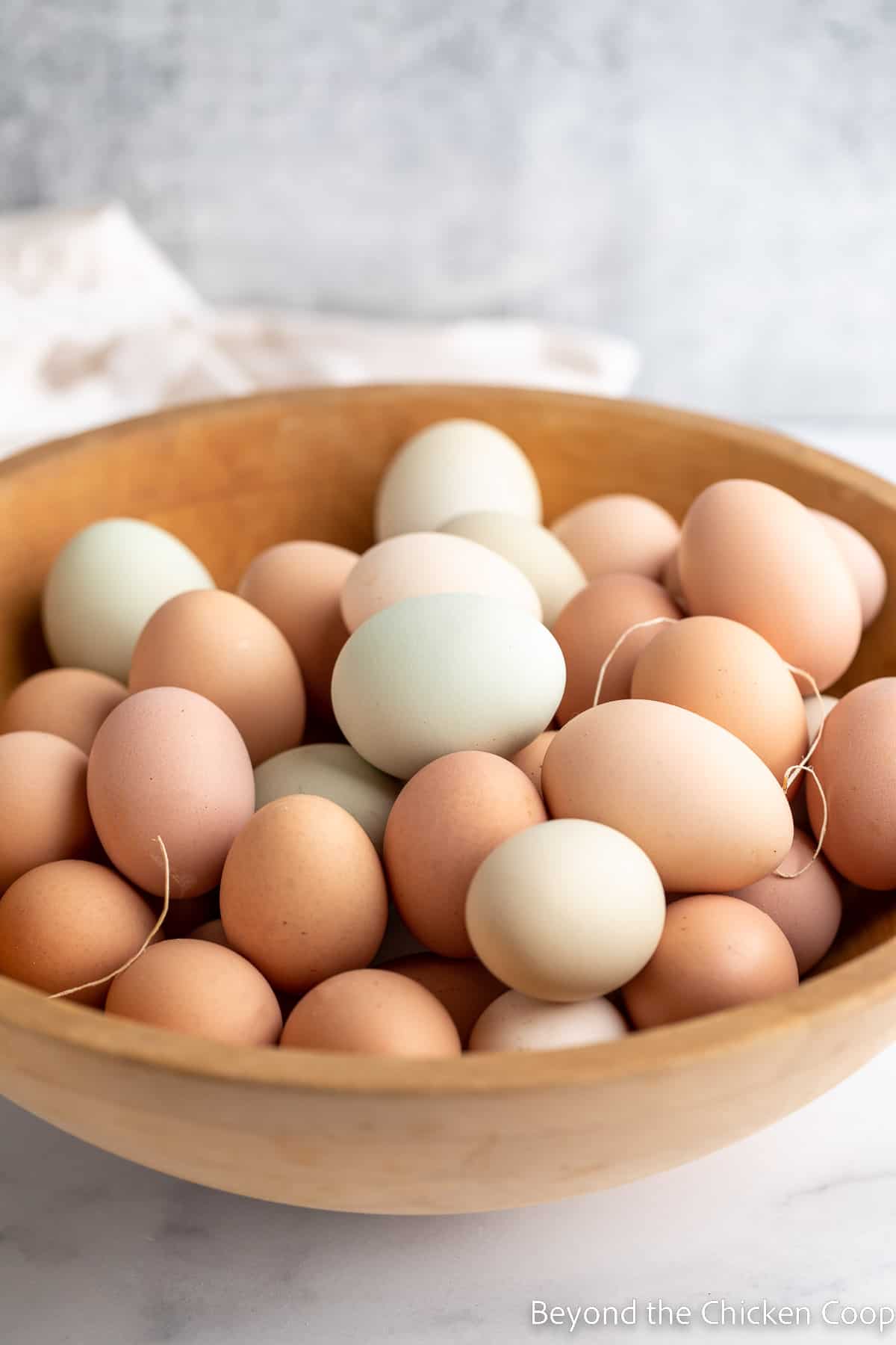 A wooden bowl filled with different colored eggs. 
