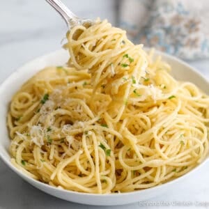 Pasta twirled around a fork and in a large white bowl.