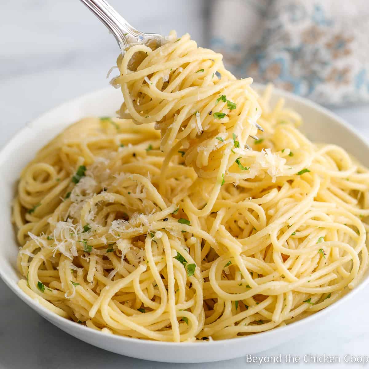 Pasta twirled around a fork and in a large white bowl. 