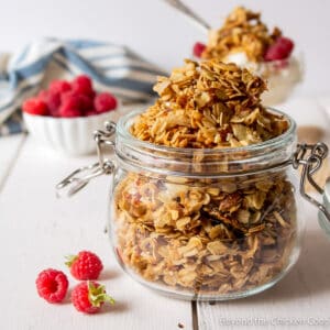 A crock filled with granola with fresh raspberries next to the crock.
