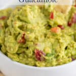A bowl filled with guacamole with bits of red tomatoes.
