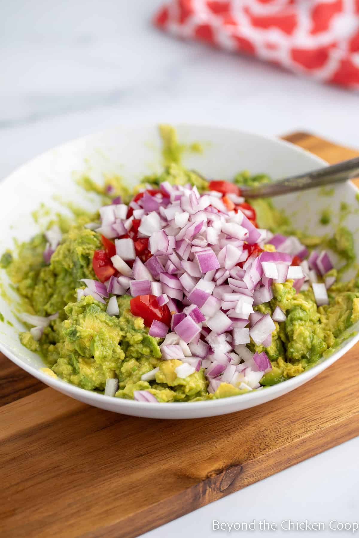 chopped onions and tomatoes on top of mashed avocados. 