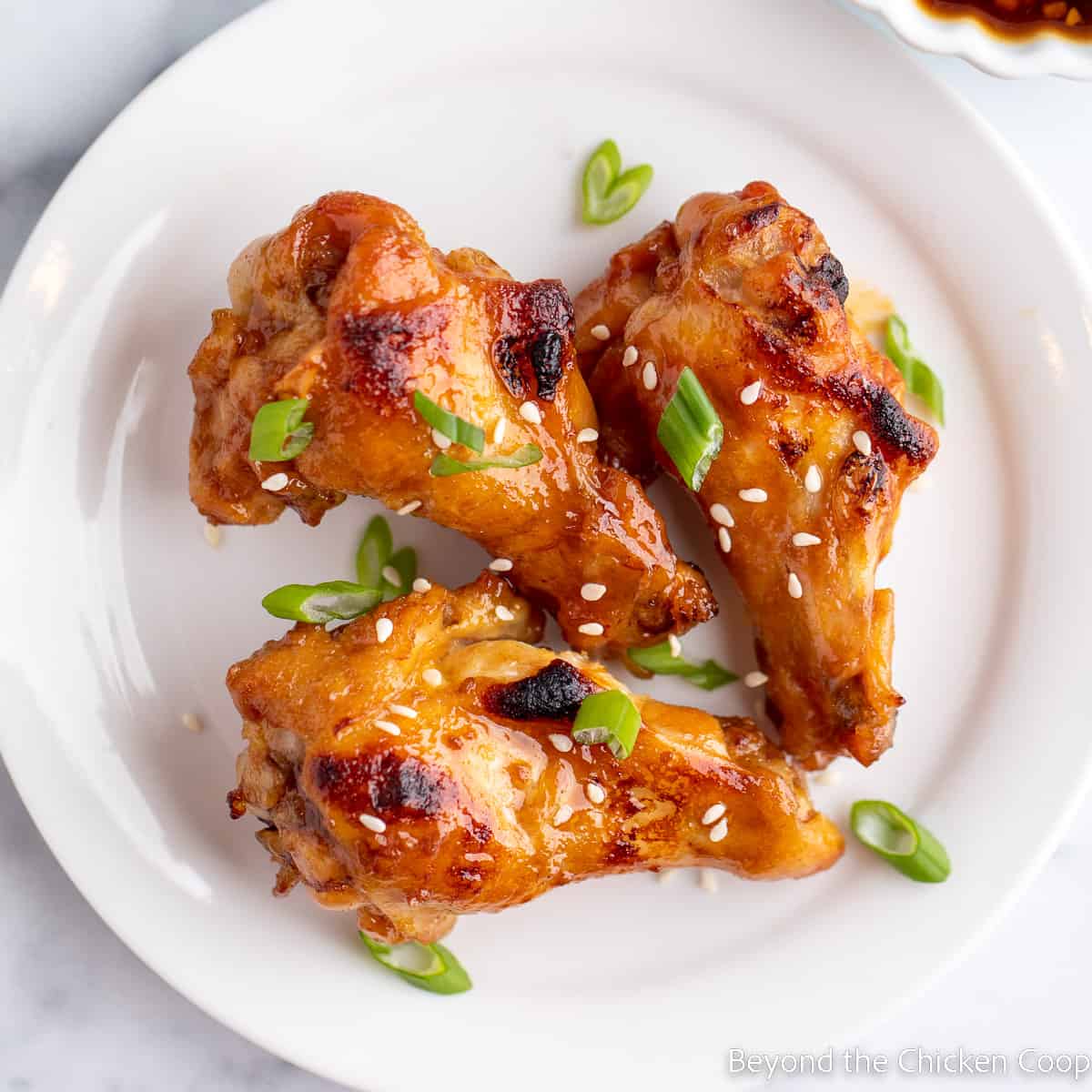 Three chicken wings with sauce on a plate.