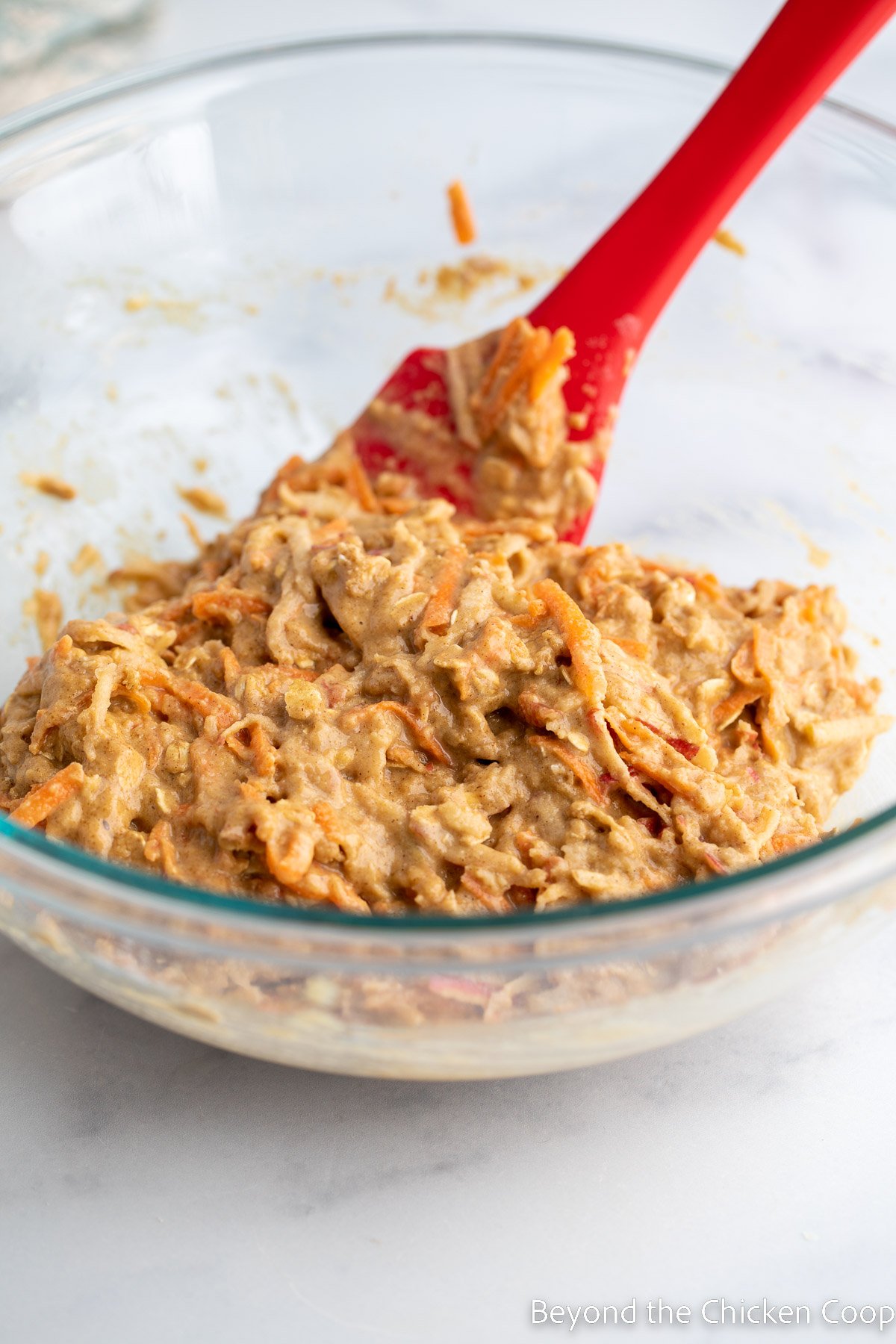Carrot and apple muffin batter in a bowl with a red spatula.