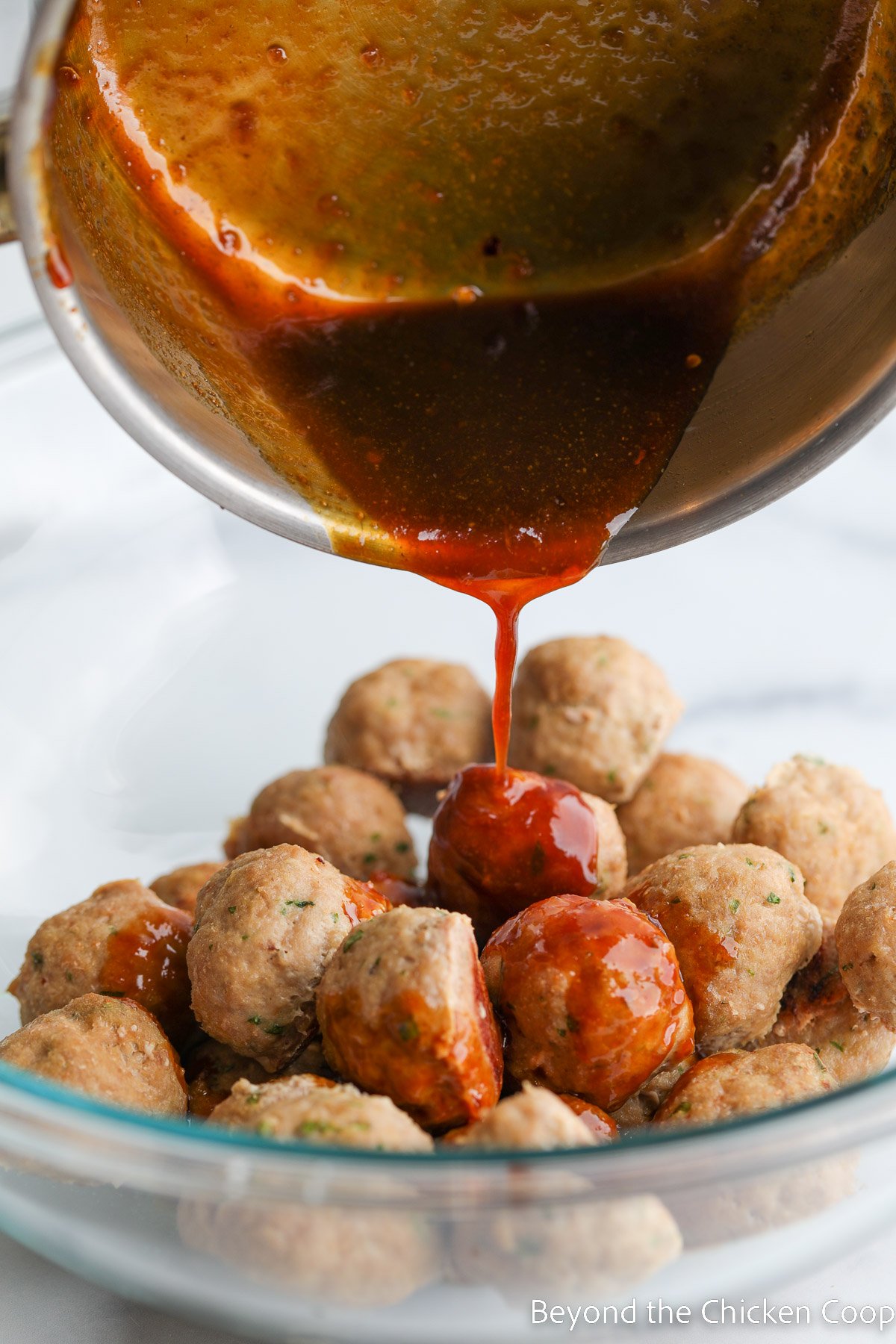 Pouring a sauce over the top of a bowl of meatballs. 