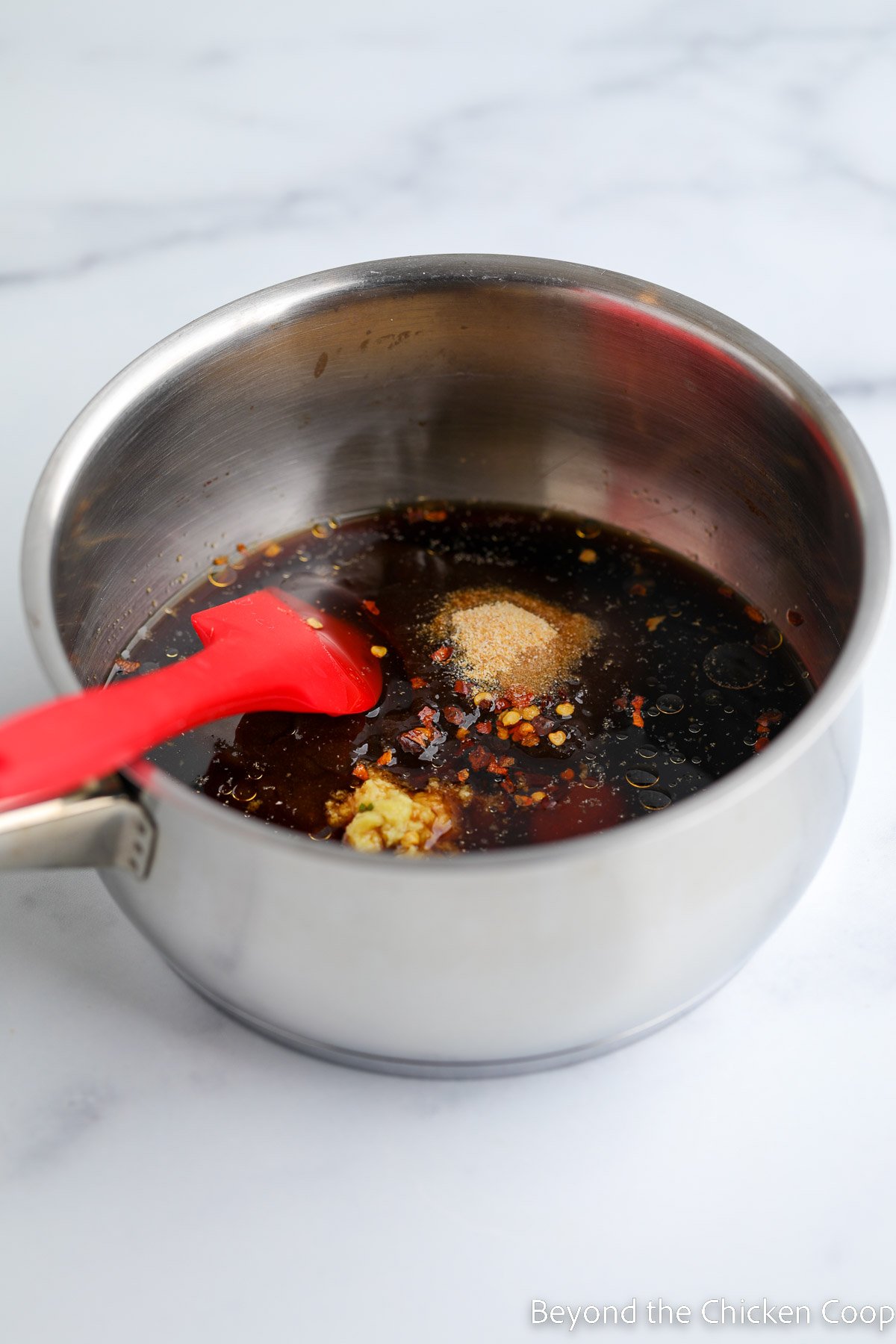 A dark sauce in a saucepan with a red spatula. 