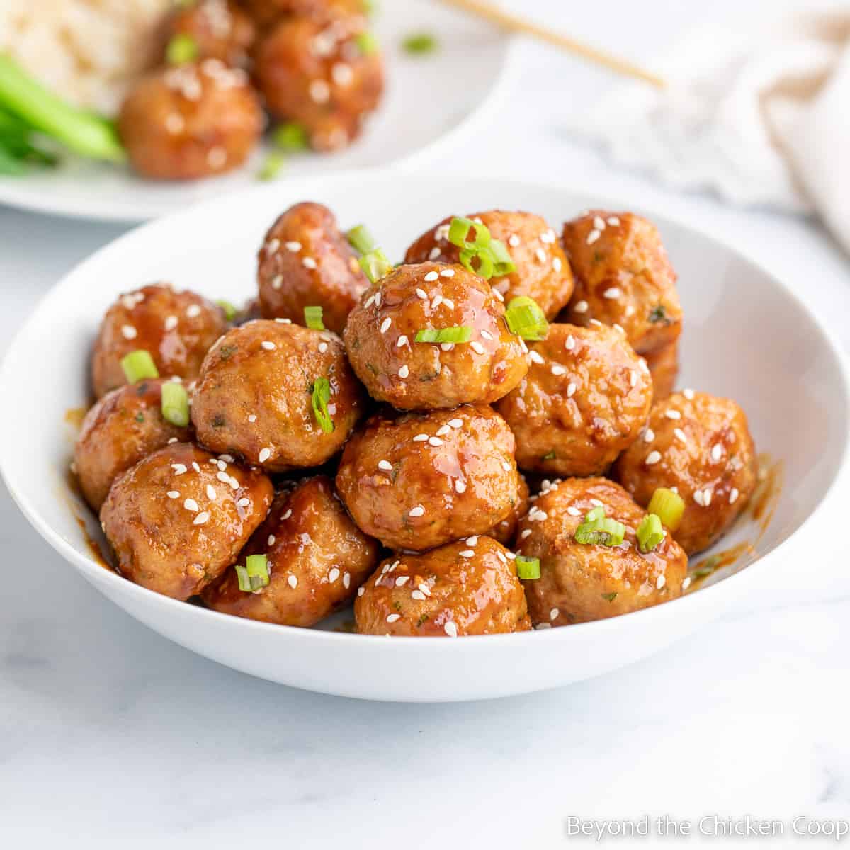 Meatballs topped with sesame seeds and green onions in a white bowl. 