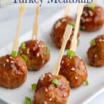 Small meatballs with toothpicks on a white platter.