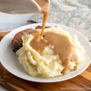Gravy pouring over a pile of mashed potatoes.