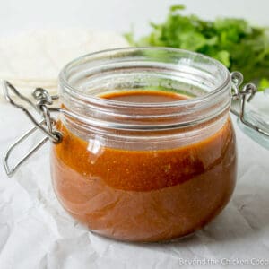 A glass crock filled with red enchilada sauce.