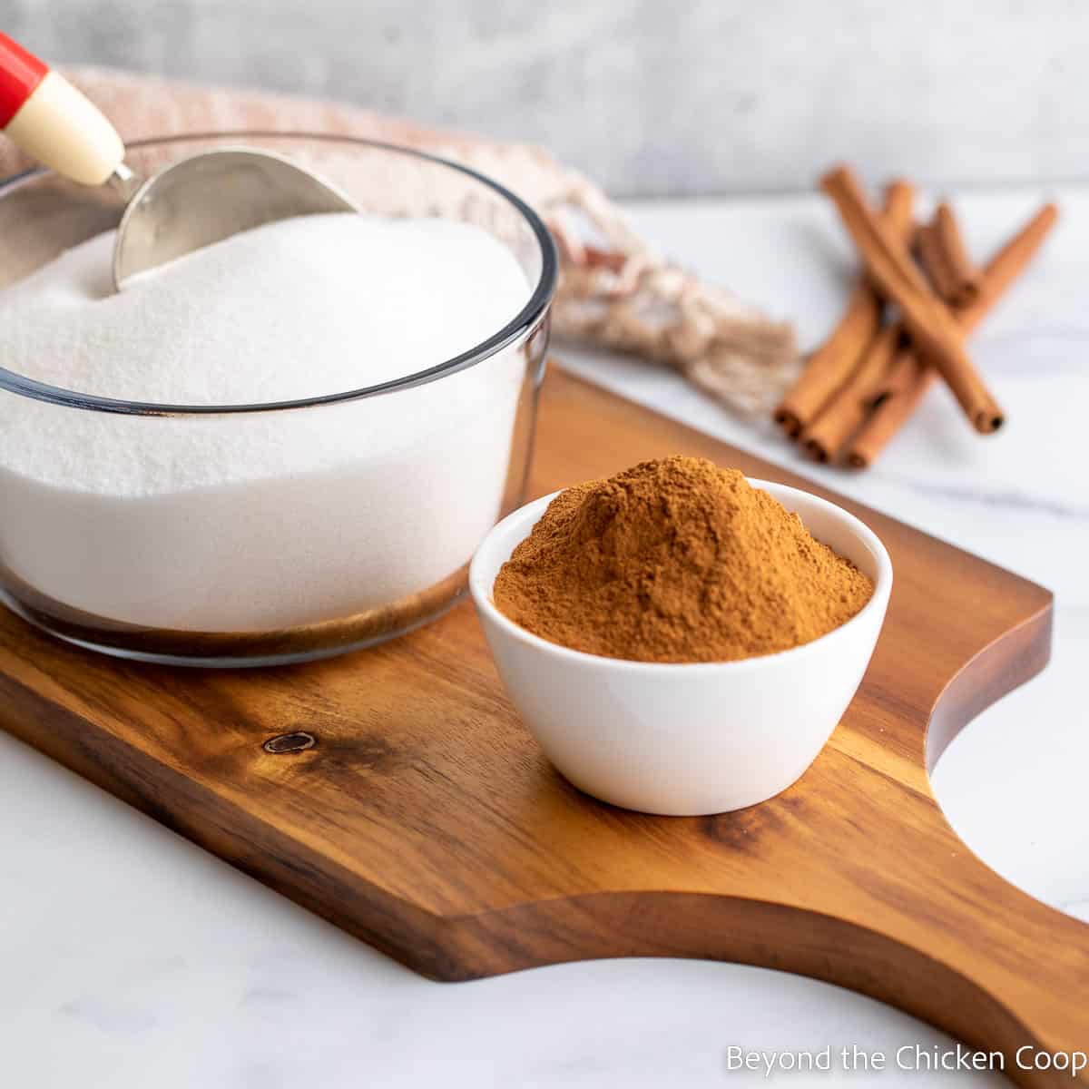 A bowl of sugar and a bowl of cinnamon on a cutting board.