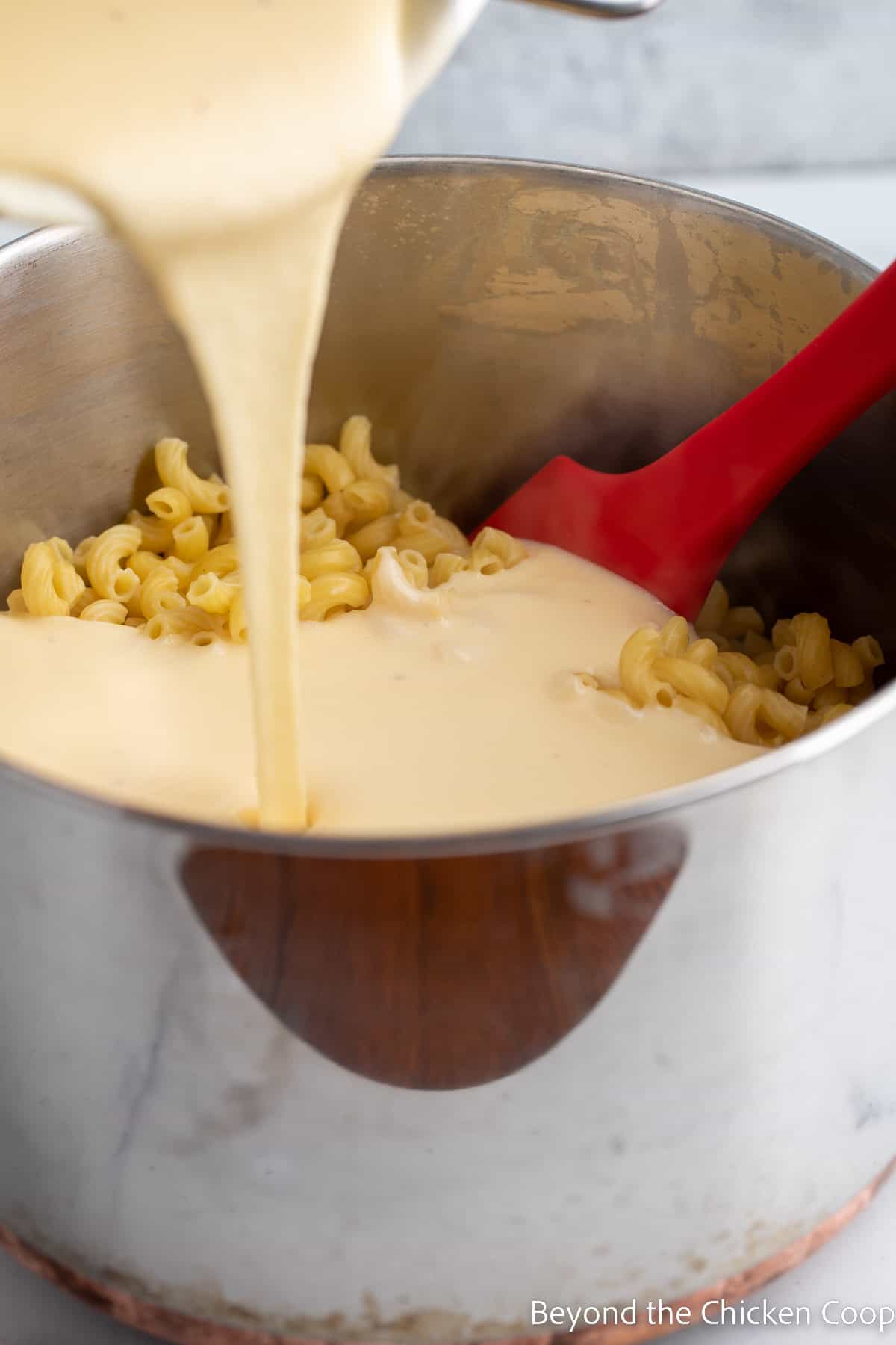 Pouring the cheese sauce over a pot of macaroni. 