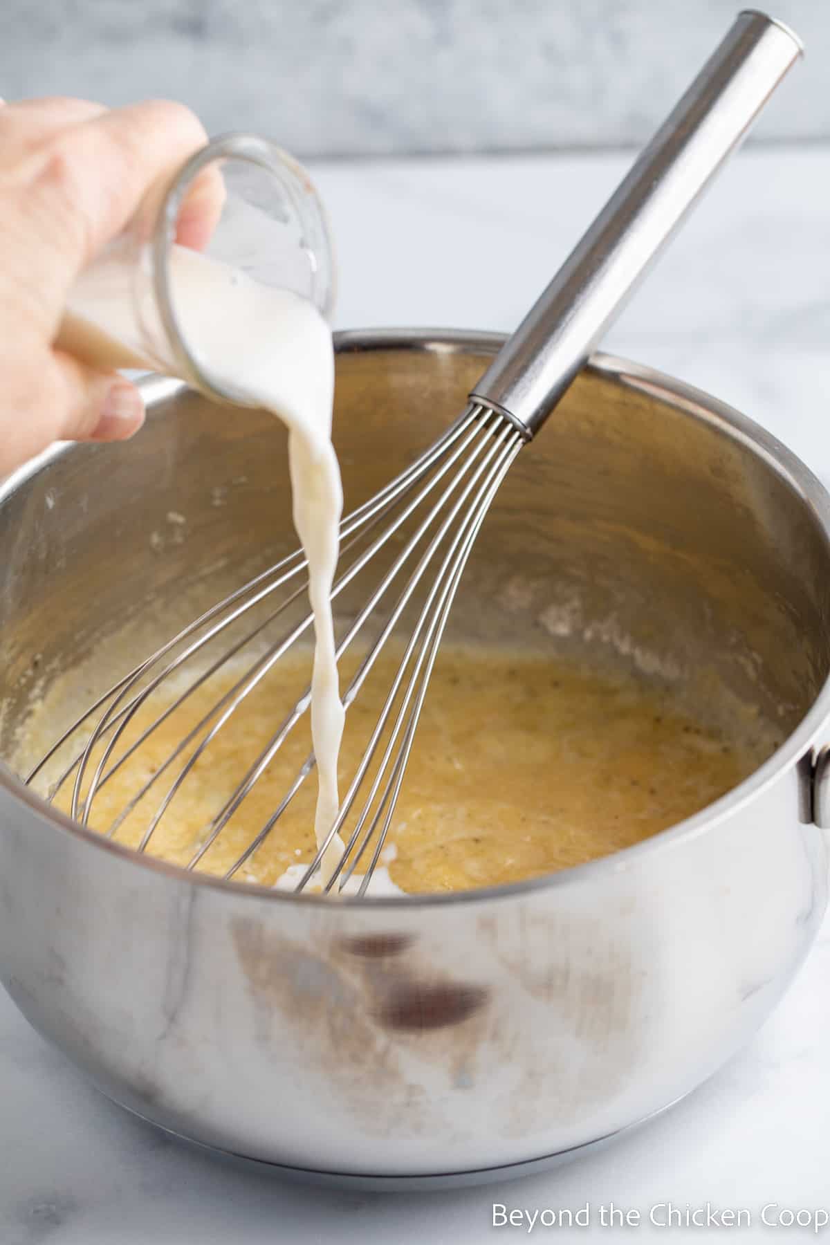 Pouring milk into a saucepan with roux. 