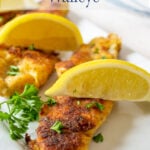 Fried fish fillets topped with lemon wedges.