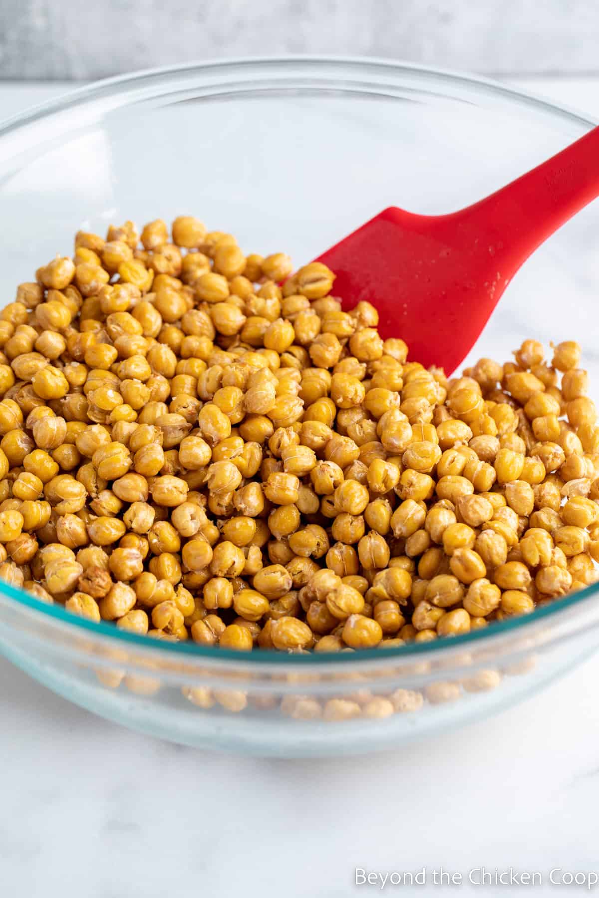 Adding olive oil and seasoning to roasted chickpeas. 