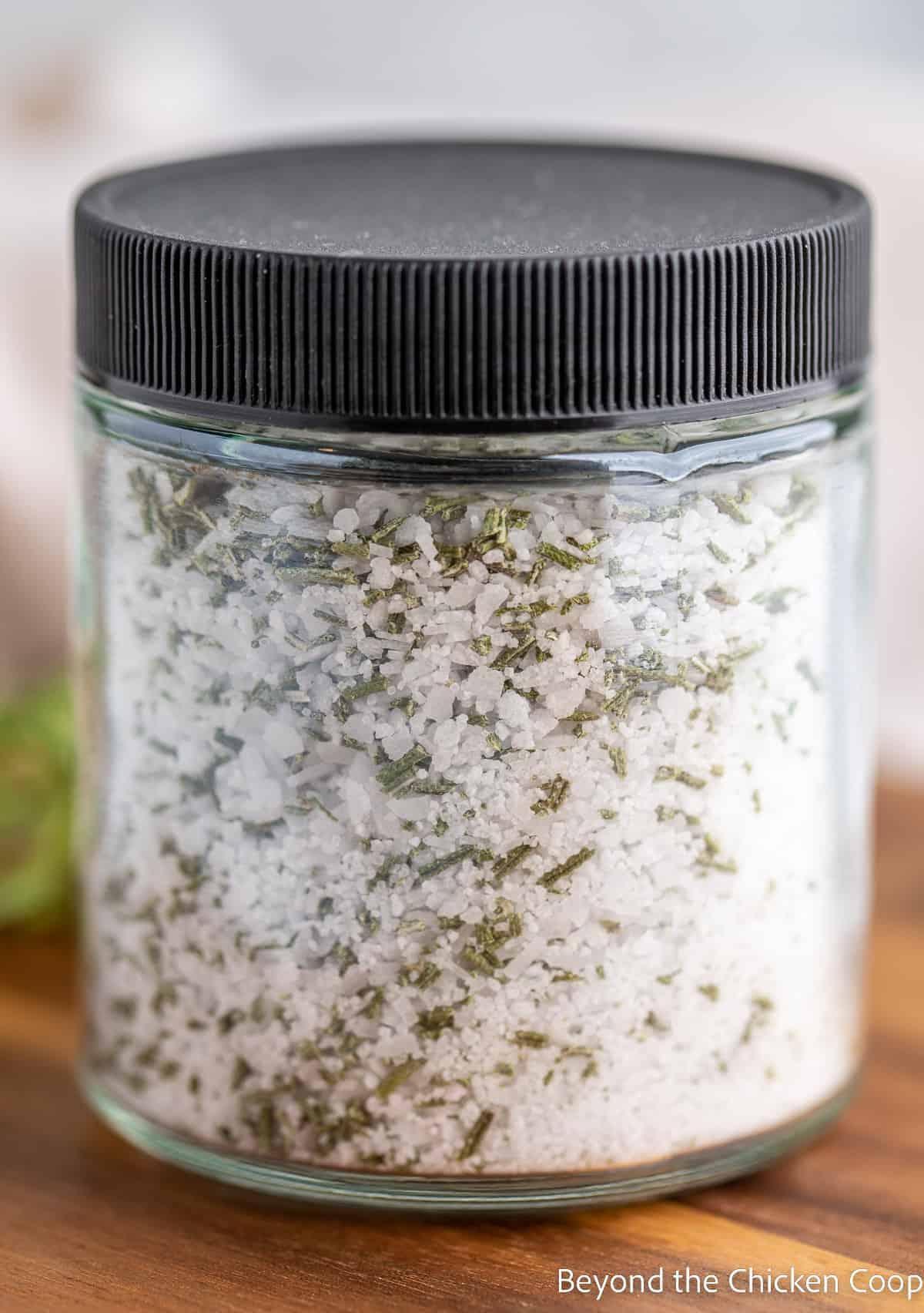 A spice jar with a black lid filled with rosemary salt. 
