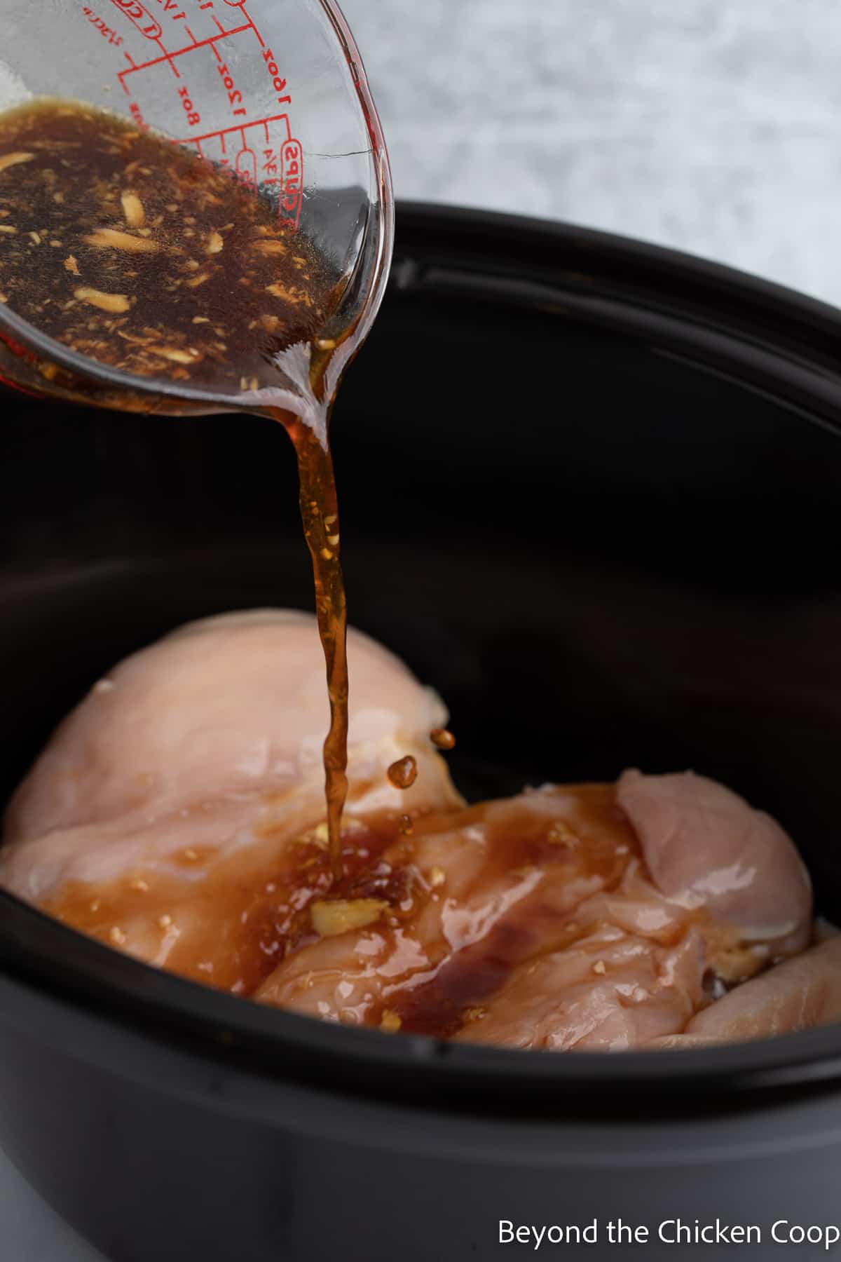 Pouring sauce over chicken in a crock pot. 