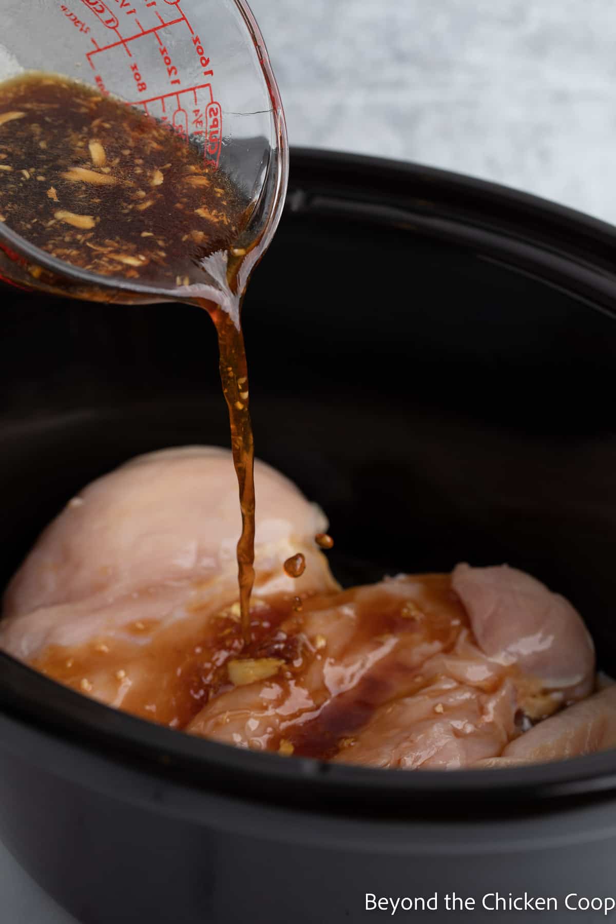 Pouring sauce over chicken in a crock pot.