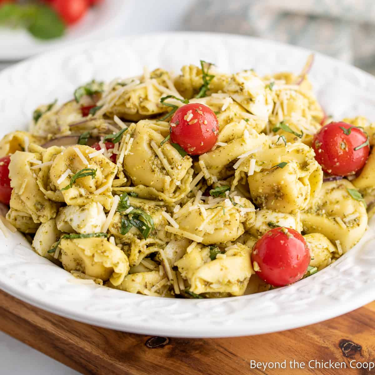 A pasta salad with tortellini and tomatoes in a white bowl.