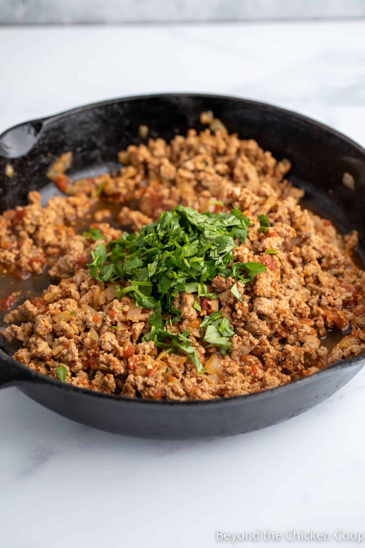 Fresh cilantro added to a pan with meat. 