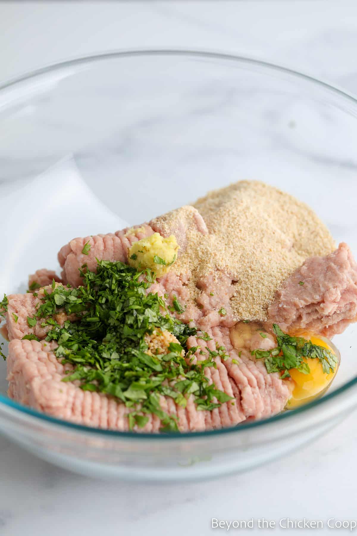 A bowl with ground turkey, fresh herbs and bread crumbs. 