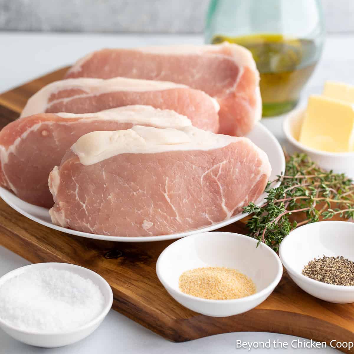 Uncooked pork chops with bowls of seasoning.